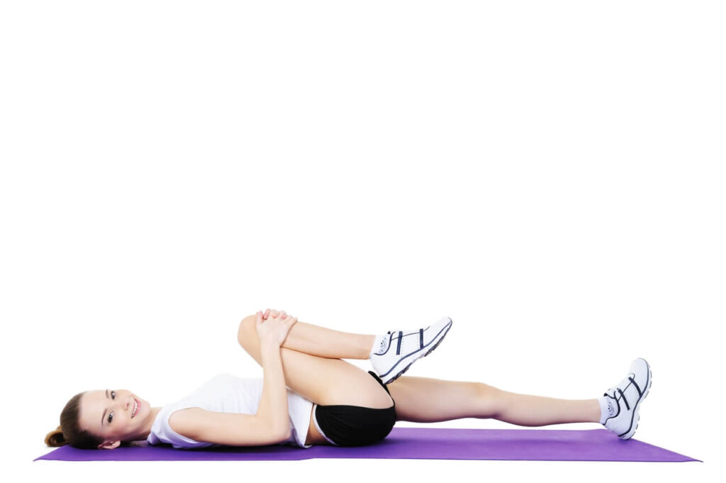 kobieta leżąc na macie wykonuje ćwiczenia na leżąco, wykonuj przyciąganie kolan do klatki piersiowej